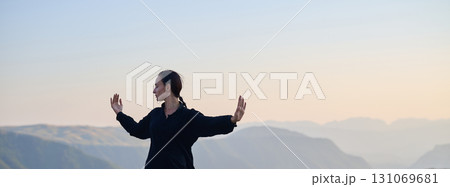 Woman practicing Tai Chi in traditional black outfit on mountain at sunrise, arms outstretched in meditation pose focusing on balance, energy, and mindfulness in nature. Woman practicing Tai Chi in traditional black outfit on mountain at sunrise, arms outstretched in meditation pose focusing on balance, energy, and mindfulness in nature. 131069681