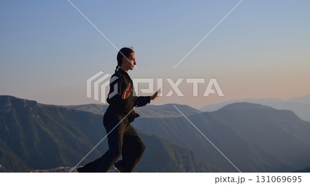 Woman practicing Tai Chi in traditional black outfit on mountain at sunrise, arms outstretched in meditation pose focusing on balance, energy, and mindfulness in nature. Woman practicing Tai Chi in traditional black outfit on mountain at sunrise, arms outstretched in meditation pose focusing on balance, energy, and mindfulness in nature. 131069695