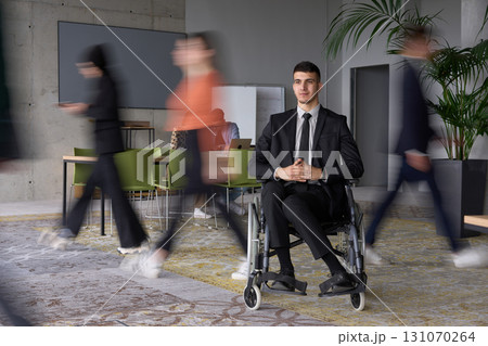 A businessman in a wheelchair navigating through a busy office, surrounded by his colleagues who are actively engaged in their work and collaboration 131070264