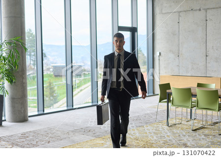 A determined businessman in a black suit confidently walks through the office, embodying professionalism and focus as he heads towards new challenges 131070422