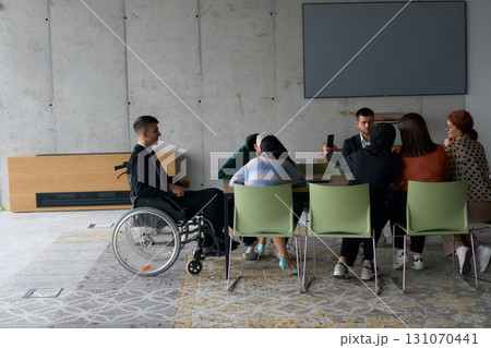 A diverse group of business professionals, including a man in a wheelchair, collaborate during a meeting in a modern office environment. A diverse group of business professionals, including a man in a wheelchair, collaborate during a meeting in a modern office environment. 131070441