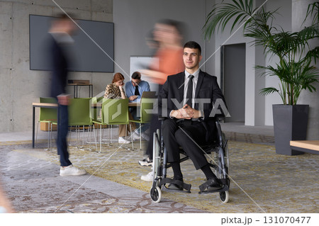 A businessman in a wheelchair navigating through a busy office, surrounded by his colleagues who are actively engaged in their work and collaboration 131070477