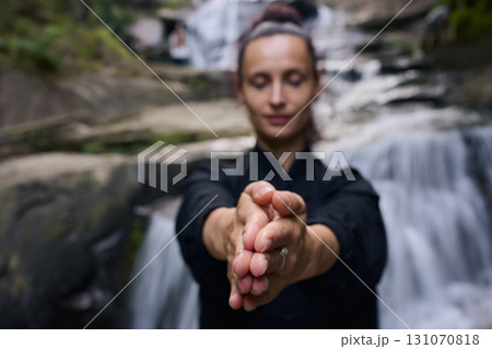 Woman practicing Tai Chi in nature, wearing a traditional black martial arts uniform, standing gracefully near a waterfall, focused on meditation and balance. Healthy lifestyle in asian culture Woman practicing Tai Chi in nature, wearing a traditional black martial arts uniform, standing gracefully near a waterfall, focused on meditation and balance. Healthy lifestyle in asian culture 131070818