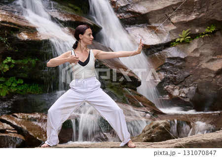 woman performing slow tai chi movements near a waterfall and river at sunset capturing harmony balance and fitness in nature 131070847