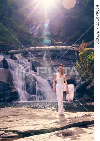 Woman doing yoga tree pose in front of waterfall at sunrise peaceful meditation in nature 131070854
