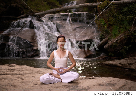 Young woman sitting in lotus pose under tropical waterfall meditating with calm strength and mindfulness fully connected to nature energy tranquility and inner balance Young woman sitting in lotus pose under tropical waterfall meditating with calm strength and mindfulness fully connected to nature energy tranquility and inner balance 131070990