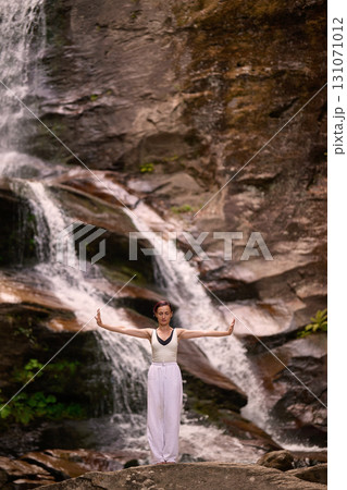 woman performing slow tai chi movements near a waterfall and river at sunset capturing harmony balance and fitness in nature 131071012