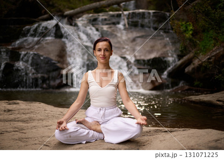 Young woman sitting in lotus pose under tropical waterfall meditating with calm strength and mindfulness fully connected to nature energy tranquility and inner balance Young woman sitting in lotus pose under tropical waterfall meditating with calm strength and mindfulness fully connected to nature energy tranquility and inner balance 131071225