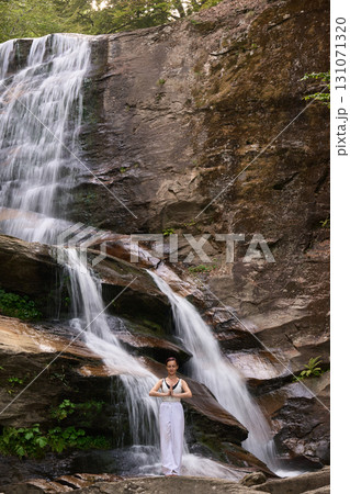 woman performing slow tai chi movements near a waterfall and river at sunset capturing harmony balance and fitness in nature 131071320