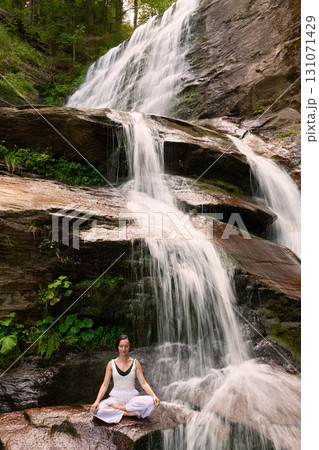 Young woman sitting in lotus pose under tropical waterfall meditating with calm strength and mindfulness fully connected to nature energy tranquility and inner balance Young woman sitting in lotus pose under tropical waterfall meditating with calm strength and mindfulness fully connected to nature energy tranquility and inner balance 131071429