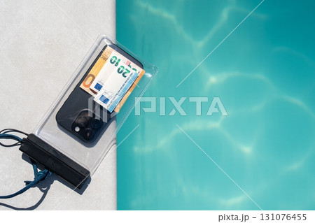 Smartphone and euro banknotes inside a transparent waterproof case with lanyard, placed on poolside edge, concept of vacation safety, protection from water, secure travel accessories. Smartphone and euro banknotes inside a transparent waterproof case with lanyard, placed on poolside edge, concept of vacation safety, protection from water, secure travel accessories. 131076455