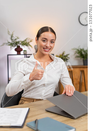 Young businesswoman ends workday closes laptop smiles gives thumbs up and lets out satisfied breath 131077023