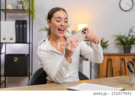 Young businesswoman plays game on smartphone during break beats level smiles and returns to reports Young businesswoman plays game on smartphone during break beats level smiles and returns to reports 131077041