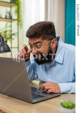 Indian man smiles after email reply on laptop nods celebrating project finish success indoors table Indian man smiles after email reply on laptop nods celebrating project finish success indoors table 131077071