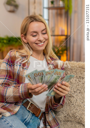 Woman counting cash money at home, smiling proudly while planning budget after lottery win or raise 131077151