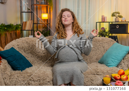 Pregnant woman meditating with closed eyes sitting at home sofa, full relaxation taking a break rest 131077168