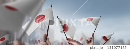 Japan flags in their hands on a blurred urban background Japan flags in their hands on a blurred urban background 131077185