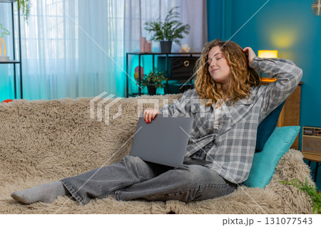Young woman on sofa yawning stretching closing laptop after long work feeling happy and satisfied 131077543