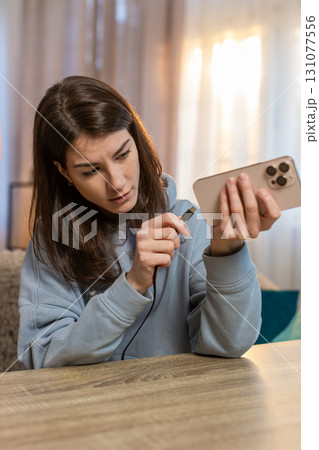 Young Caucasian woman repeatedly plugging and unplugging broken charger into smartphone at table 131077556