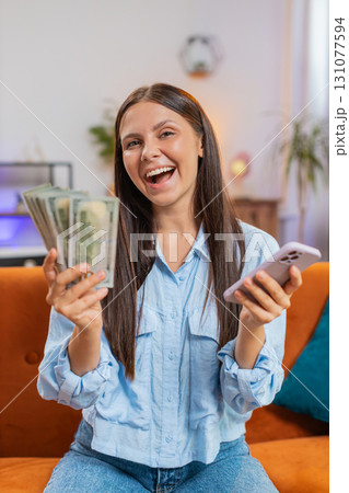 Smiling happy rich young woman counting money dollar cash use smartphone, income, saves, lottery win Smiling happy rich young woman counting money dollar cash use smartphone, income, saves, lottery win 131077594