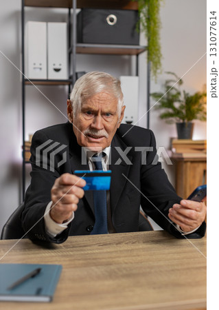 Caucasian angry senior businessman trying to pay online with smartphone blocked credit card at home 131077614