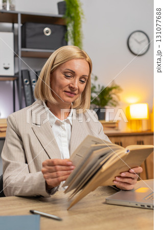 Mature businesswoman reading interesting book smiling enjoying literature taking a rest after work Mature businesswoman reading interesting book smiling enjoying literature taking a rest after work 131077688