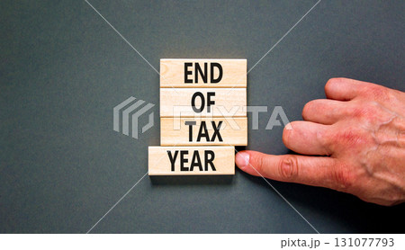 End of tax year symbol. Concept words phrase End of tax year on beautiful wooden blocks. Beautiful grey paper background. Businessman's hand. Business End of tax year concept. Copy space. End of tax year symbol. Concept words phrase End of tax year on beautiful wooden blocks. Beautiful grey paper background. Businessman's hand. Business End of tax year concept. Copy space. 131077793