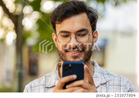 Indian young man using smartphone typing text messages in social media application online on street 131077804