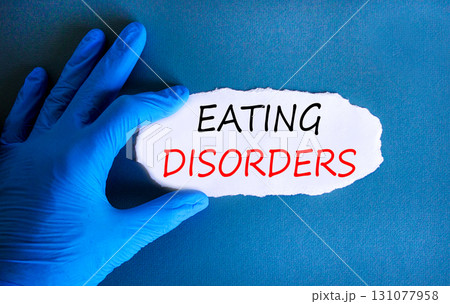 Eating disorders symbol. Concept words Eating disorders on beautiful white paper. Doctor's hand in blue medical glove. Beautiful blue background. Medical healthy lifestyle eating disorders concept. Eating disorders symbol. Concept words Eating disorders on beautiful white paper. Doctor's hand in blue medical glove. Beautiful blue background. Medical healthy lifestyle eating disorders concept. 131077958