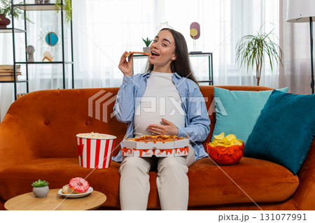 Pregnant woman eating unhealthy junk fatty fast food pizza popcorn crisp watching movie at home Pregnant woman eating unhealthy junk fatty fast food pizza popcorn crisp watching movie at home 131077991