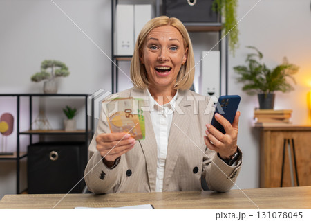 Mature businesswoman counting money euro cash using smartphone calculator app at home office desk 131078045