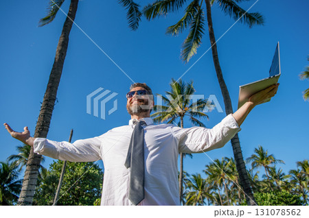 Businessman boss with laptop. Business man using laptop near palm tree. Business trip. Man freelance work online at beach. Businessman on summer vacation. Online freelance work. Flexible schedule Businessman boss with laptop. Business man using laptop near palm tree. Business trip. Man freelance work online at beach. Businessman on summer vacation. Online freelance work. Flexible schedule 131078562