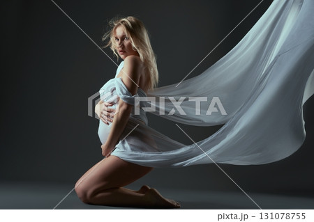 Pregnant woman in sagging fabric sitting on her knees 131078755