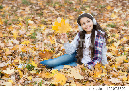 Thoughtful beauty. autumn kid fashion. inspiration. happy childhood. back to school. girl among maple leaves relax in park. fall in forest. enjoy music in earphones. education online and e-learning 131078792