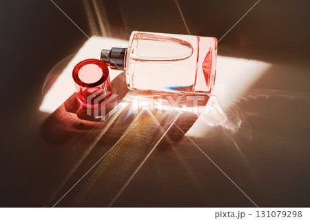 Pink perfume bottle on the light background in the rays of sun with highlights. 131079298