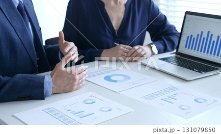 Businesspeople reviewing financial documents, collaborating over laptop screen, analyzing market charts for strategic corporate planning. Business people and finance concept 131079850