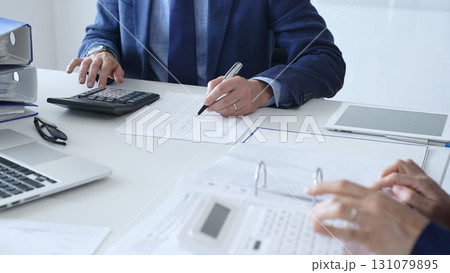 Close up of female accountant hands using calculator while collaborating with male colleague in office, calculating taxes and analyzing financial data. Audit and taxes in business 131079895