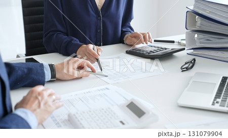 Business team analyzing financial documents, using calculators and laptop, working together on project in modern office. Audit and taxes concept 131079904