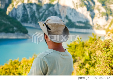 A man wearing a hat enjoys the autumn mountain landscape while traveling in Montenegro. Scenic nature, adventure, and travel lifestyle concept. A man wearing a hat enjoys the autumn mountain landscape while traveling in Montenegro. Scenic nature, adventure, and travel lifestyle concept. 131080052