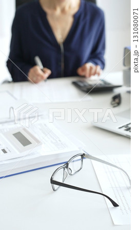 Professional analyzing financial data, writing notes near laptop, magnifying glass, documents, binders on workplace desk. Audit and taxes concept Professional analyzing financial data, writing notes near laptop, magnifying glass, documents, binders on workplace desk. Audit and taxes concept 131080071