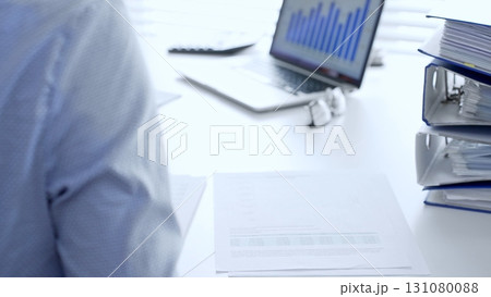 Corporate professionals reviewing financial documents, working collaboratively at white desk with blue folder stack, highlighting teamwork and business productivity. Audit and taxes in business Corporate professionals reviewing financial documents, working collaboratively at white desk with blue folder stack, highlighting teamwork and business productivity. Audit and taxes in business 131080088