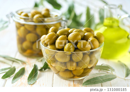 pickled green olives in a transparent glass bowl on a white wooden table, selective focus. 131080185