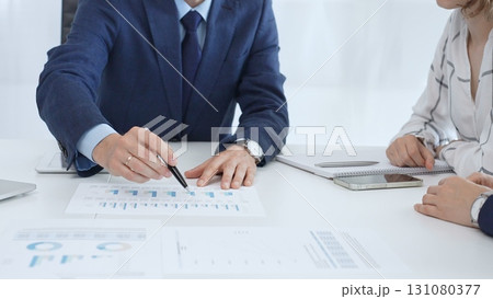 Business team engaging in a corporate meeting, discussing strategies while analyzing financial charts and graphs on a digital tablet alongside printed documents 131080377