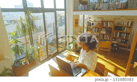 Woman working on laptop in sunlit modern apartment with plants a 131080383