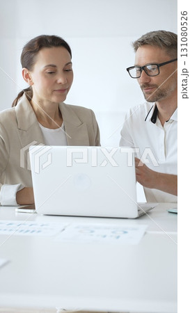 Businessman and adult businesswoman reviewing marketing analytics on laptops, working together strategically in contemporary workplace with minimalist interior design and collaborative atmosphere Businessman and adult businesswoman reviewing marketing analytics on laptops, working together strategically in contemporary workplace with minimalist interior design and collaborative atmosphere 131080526