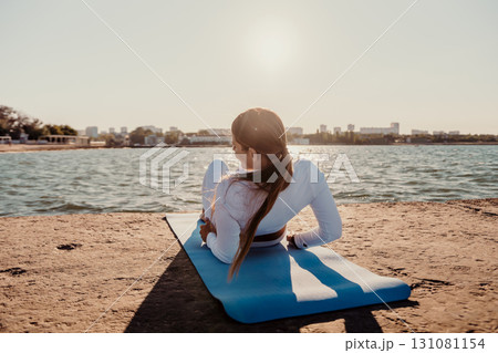 Yoga Beach Workout Woman - A woman practices yoga on a blue mat at the beach at sunset. Yoga Beach Workout Woman - A woman practices yoga on a blue mat at the beach at sunset. 131081154