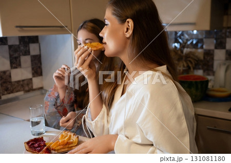 Women Kitchen Snack Food: Two women enjoy a snack of pastries in their kitchen, likely during the evening. Women Kitchen Snack Food: Two women enjoy a snack of pastries in their kitchen, likely during the evening. 131081180