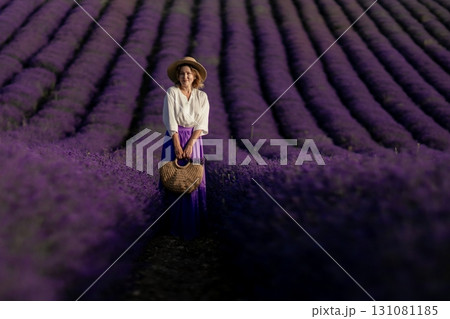 A woman stands in a field of lavender flowers, holding a basket 131081185