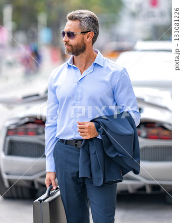Corporate business. Luxury businessman in suit. Business leader portrait. Successful businessman walking with briefcase at parking. Businessman hold briefcase. Mature businessman in suit Corporate business. Luxury businessman in suit. Business leader portrait. Successful businessman walking with briefcase at parking. Businessman hold briefcase. Mature businessman in suit 131081226