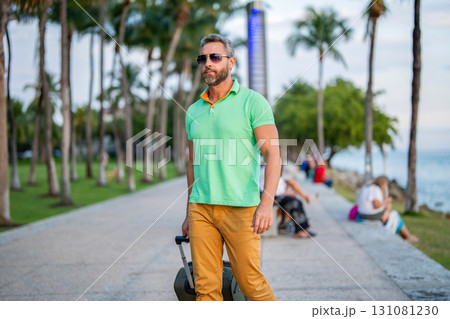 Tourist on summer vacation. Traveler luggage for summer trip. Summer tour. Traveler enjoy summer trip. Hispanic tourist traveler walking on tropical city. Tourist with suitcase. Man 40s traveler 131081230